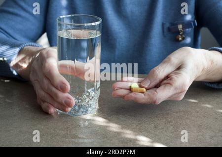 Primo piano di una donna anziana che tiene le pillole e un bicchiere di acqua potabile. La donna anziana sta per prendere farmaci per le malattie. Problemi di salute nel vecchio Foto Stock