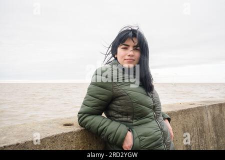 Ritratto di una giovane turista venezuelana latina, con giacca verde per il freddo, in piedi sul molo del porto di olivos a Buenos Aires, calma loo Foto Stock