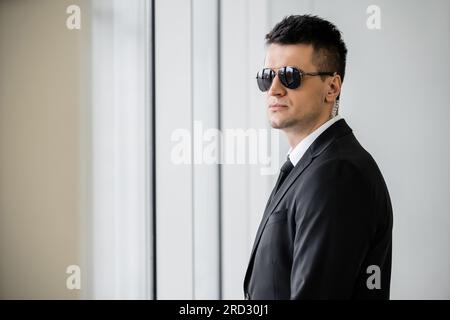 copricapo professionale, bodyguard work, bell'uomo con occhiali da sole e tuta nera con cravatta, sicurezza in hotel, gestione della sicurezza, sorveglianza e vi Foto Stock