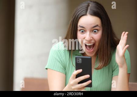 Donna entusiasta che guarda contenuti straordinari al telefono per strada Foto Stock