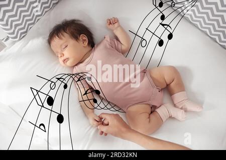 Canzoni ninnananna. Madre che tiene la mano del bambino addormentato sul letto, vista dall'alto. Illustrazione di note musicali volanti intorno al bambino Foto Stock