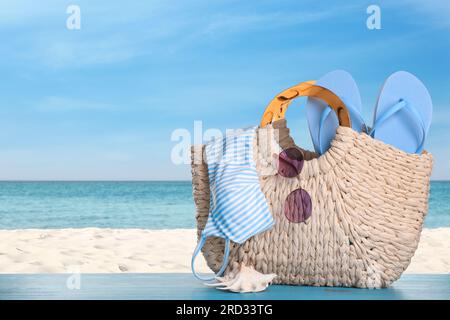 Borsa con zona bikini e accessori sulla soleggiata spiaggia dell'oceano, spazio per messaggi. Vacanze estive Foto Stock