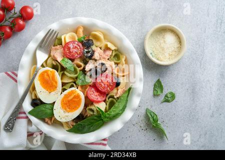 Insalata di pasta italiana. Orecchiette con tonno, ciliegia di pomodoro, oliva, basilico e parmigiano in piatto su fondo di pietra grigia o cemento. Tradi Foto Stock