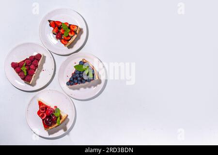Menu estivo di cottura in caffè, porzione di cheesecake dolce a fette con vari condimenti, marmellata e frutti di bosco - fragole, mirtilli, lamponi, ecc. Foto Stock