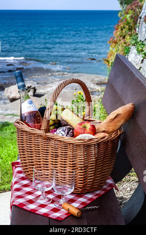 Cestino da picnic all'aperto su panchina con ampia vista sul mare, paesaggio temperato a Doëlan Finistere Bretagna, Francia Foto Stock