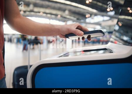 Mano dell'uomo durante l'uso della macchina di check-in self-service. Il passeggero esegue la scansione del biglietto sullo smartphone presso il terminal dell'aeroporto. Foto Stock