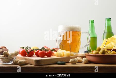 Tazza da birra su panchina di legno e spuntini intorno con sfondo bianco isolato. Vista frontale. Foto Stock