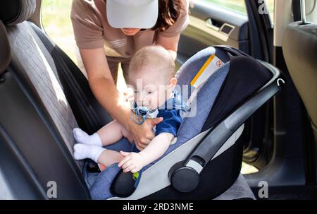 Una giovane madre mette il bambino su un seggiolino per auto e allaccia le cinture di sicurezza. Sicurezza dei neonati durante la guida. Primo piano Foto Stock