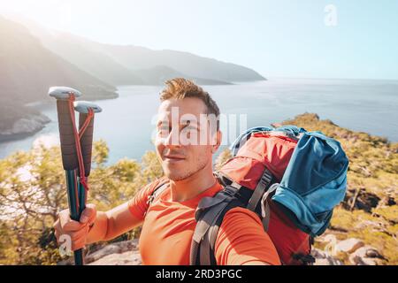 Uomo felice con bastoni da trekking che scatta selfie ammirando la vista panoramica della costa marina. Visita alla Lycian Way Foto Stock