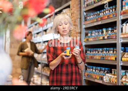 La donna anziana sceglie pigmenti multicolore per i suoi futuri piatti in argilla o ceramica in un negozio specializzato Foto Stock