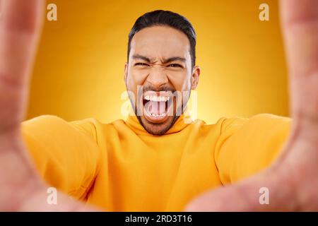 Urla, ritratto e selfie di un uomo arrabbiato in studio isolato su uno sfondo giallo. Faccia, urla e persona asiatica che scatta foto del profilo per Foto Stock