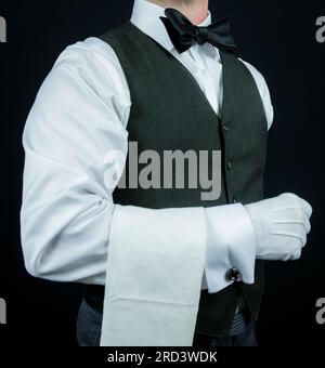 Ritratto di maggiordomo o cameriere in giubbotto e guanti bianchi in piedi con un'attenzione elegante. Concetto di ospitalità professionale. Foto Stock
