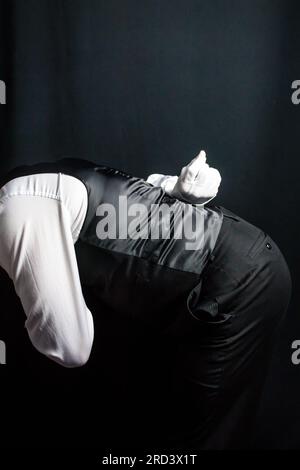 Ritratto di maggiordomo o cameriere nel giubbotto e guanti bianchi che si inchinano in un servizio cortese. Concetto di ospitalità professionale. Foto Stock