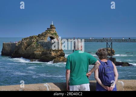 Biarritz, Francia, luglio 2023 Una coppia di turisti ha ammirato il Rocher de la Vierge e il suo ponte, la Passerelle Eiffel al largo della Plage du Port vie Foto Stock