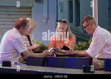 Biarritz, Francia, luglio 2023 Un gruppo turistico controlla i propri smartphone in un bar in Rue du Port-Vieux, Biarritz Foto Stock