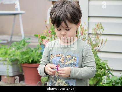 Il curioso bambino sta giocando con un fiore viola nel cortile Foto Stock