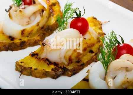 Seppia fritta su un grill con ananas e pomodori ciliegini è un piatto gustoso Foto Stock