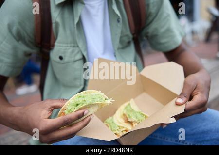 Primo piano di Young Man Eating Taco al Outdoor Street Food Stall Foto Stock