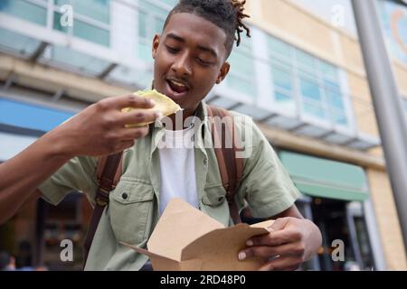 Young Man che mangia Taco all'Outdoor Street Food Stall Foto Stock