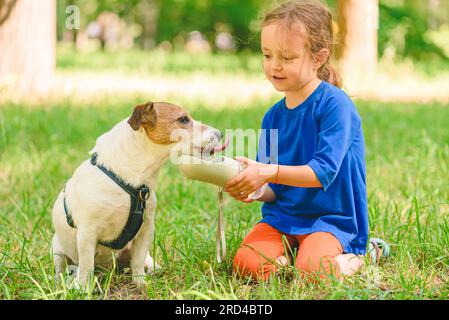 Nelle calde giornate estive, le ragazze che annaffiano il cane nel parco. Acqua potabile per cani da una speciale bottiglia per animali domestici. Foto Stock