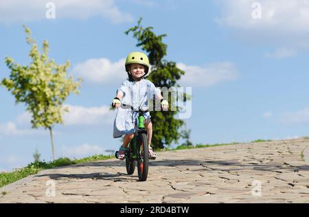 Una bambina felice che va in bicicletta in discesa nel parco con il cielo blu sullo sfondo Foto Stock