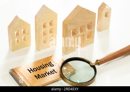 Case in miniatura in legno, mercato delle abitazioni scritto. Lente d'ingrandimento, previsione di nuove tendenze e cambiamenti nelle tendenze degli alloggi. Analisi del mercato immobiliare, Mortg Foto Stock