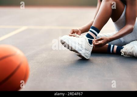 Non voglio andare in tribunale. Foto ritagliata di una sportiva irriconoscibile seduta sul campo e legando i lacci delle scarpe prima di giocare a una partita di Foto Stock