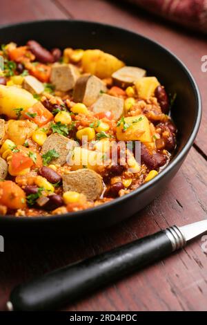 Stufato Vegan Cowboy con cipolla, peperone, granuli TVP, pomodori tritati, fagioli rossi, patate, mais e hot dog vegani Foto Stock