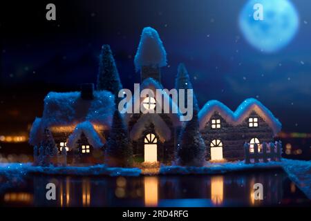 Una piccola città vicino a uno stagno in una notte invernale illuminata dalla luna. Decorazione natalizia Foto Stock