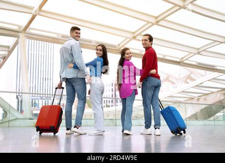 Due coppie romantiche abbracciate in posa con le valigie nell'aeroporto moderno Foto Stock