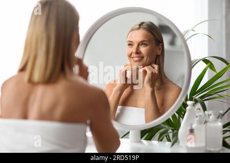 Concetto di Facebuilding. Bella donna di mezza età che guarda allo specchio e massaggia il viso Foto Stock