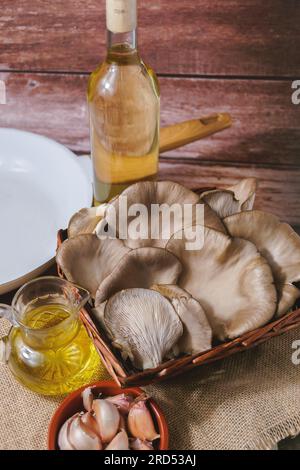 Funghi selvatici o (Pleurotus eryngii) in un cestino di vimini con ingredienti per cucinare, aglio e olio d'oliva Foto Stock