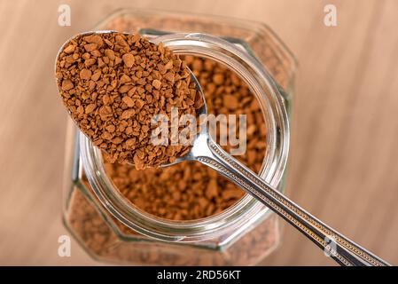 Caffè granulare istantaneo in un cucchiaio sopra un vaso su uno sfondo di legno. Spazio di copia. Foto Stock