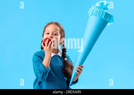 Bambina felice con il cono scolastico che mangia mela fresca su sfondo blu Foto Stock