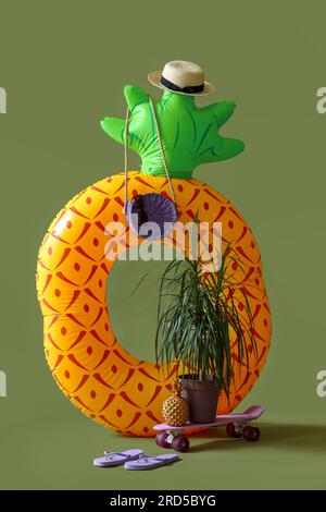 Anello gonfiabile a forma di ananas con skateboard e accessori da spiaggia su sfondo verde. Concetto di viaggio Foto Stock