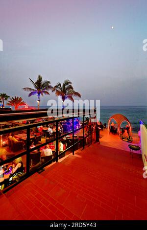 Lanzarote Isole Canarie Puerto del Carmen, il ristorante Cafe la Ola, sulla strada principale, si affaccia sulla spiaggia e sulle palme con un blu chiaro e rosso Foto Stock