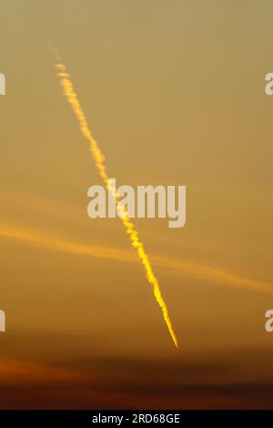 Sentiero dei vapori dell'aeroplano (contrail) attraverso il cielo dorato al tramonto. Foto Stock