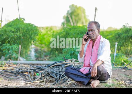 felice contadino seduto in terra a parlare al telefono , vecchio contadino indiano Foto Stock