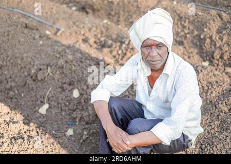 Triste agricoltore, anziano contadino seduto nel terreno e perso nel pensiero molto profondamente. Indossa abiti indiani tradizionali Foto Stock