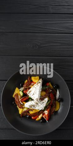 Insalata greca fresca. Piatto con feta, pomodori, cetrioli, pepe rosso, olive nere, pomodori secchi e cipolla su tavola di legno nero. Copia Foto Stock