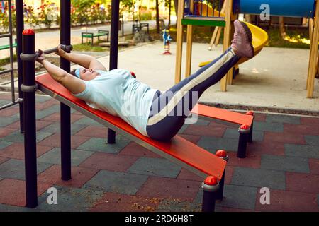 Donna in sovrappeso che fa esercizi fisici su attrezzature per l'allenamento in campo sportivo Foto Stock