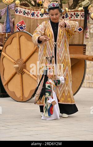 Donna uzbeka che tiene un burattino durante una performance per strada a Khiva, Uzbekistan Foto Stock