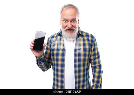 pensionato anziano con i capelli grigi, barba in camicia, regge uno smartphone con un mockup su sfondo bianco Foto Stock