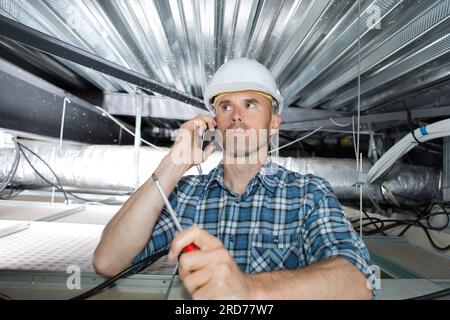 uomo al telefono che controlla il filtro dell'aria condizionata nel soffitto Foto Stock