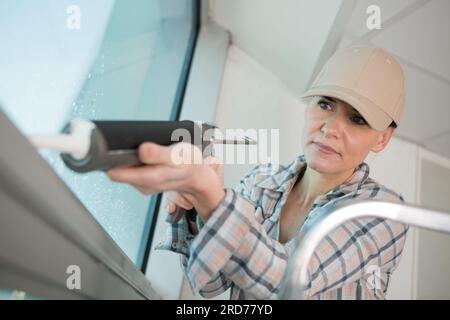 donna che utilizza una pistola per sigillante al silicone sul cantiere Foto Stock