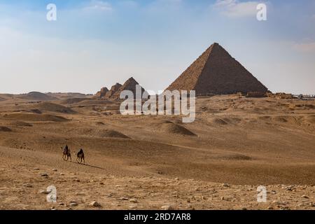 Gli uomini su cammelli attraversano le sabbie del deserto del Sahara con lo splendido sfondo delle piramidi di Giza, in Egitto. Foto Stock