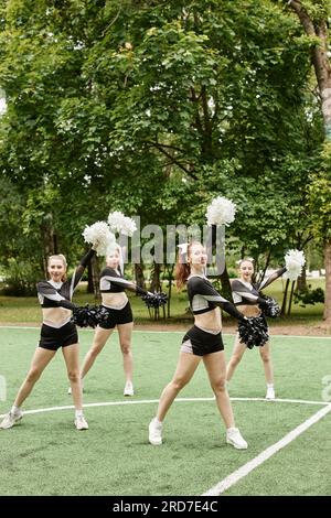 Immagine verticale di bellissime ragazze della squadra di cheerleading che ballano con pompon all'aperto Foto Stock