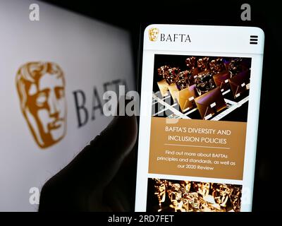 Persona in possesso di cellulare con pagina Web dei British Academy Film Awards (BAFTA) sullo schermo davanti al logo. Concentrarsi sul centro del display del telefono. Foto Stock
