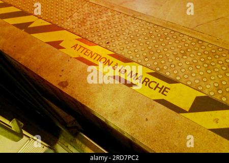 Cartello di avvertimento a strisce gialle e nere dipinto sul bordo di una banchina della metropolitana di Parigi che recita in francese "Attention à la marche", che significa in Foto Stock