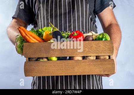 Concetto di shopping del mercato biologico agricolo, scatola di legno con estate, verdure crude e frutta autunnali, mani contadine su sfondo bianco Foto Stock